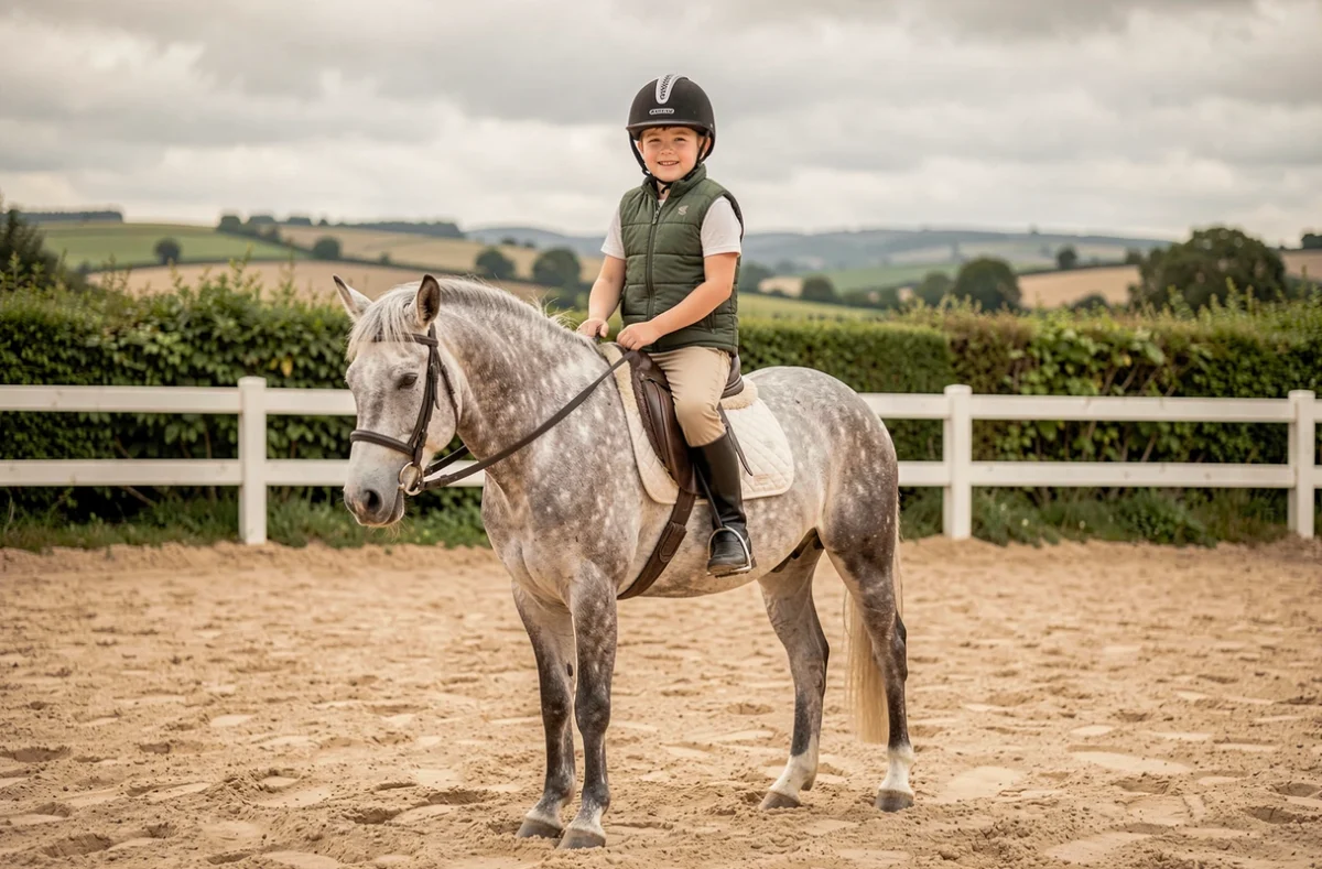 Enfant à cheval sur un poney gris dans un manège extérieur, démontrant les bienfaits de l'équitation pour les jeunes cavaliers